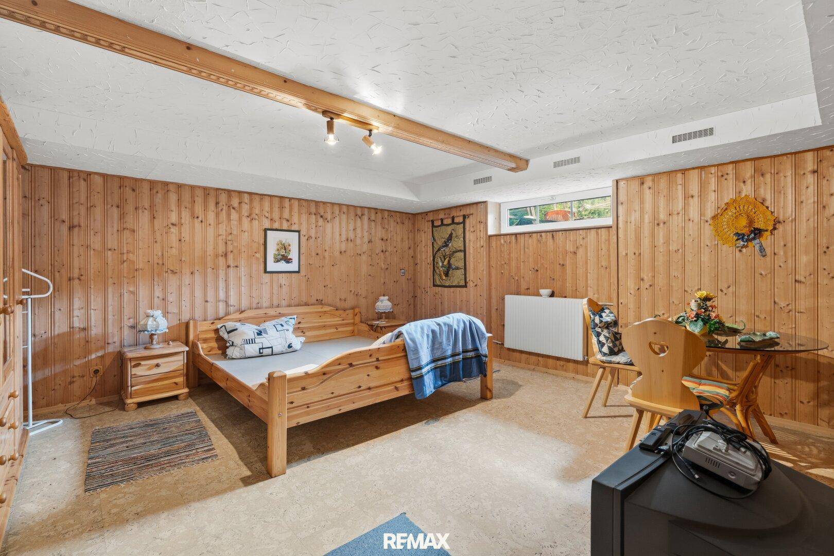 Gemütliches Schlafzimmer im Keller mit Holzvertäfelung und kleinem Fenster.