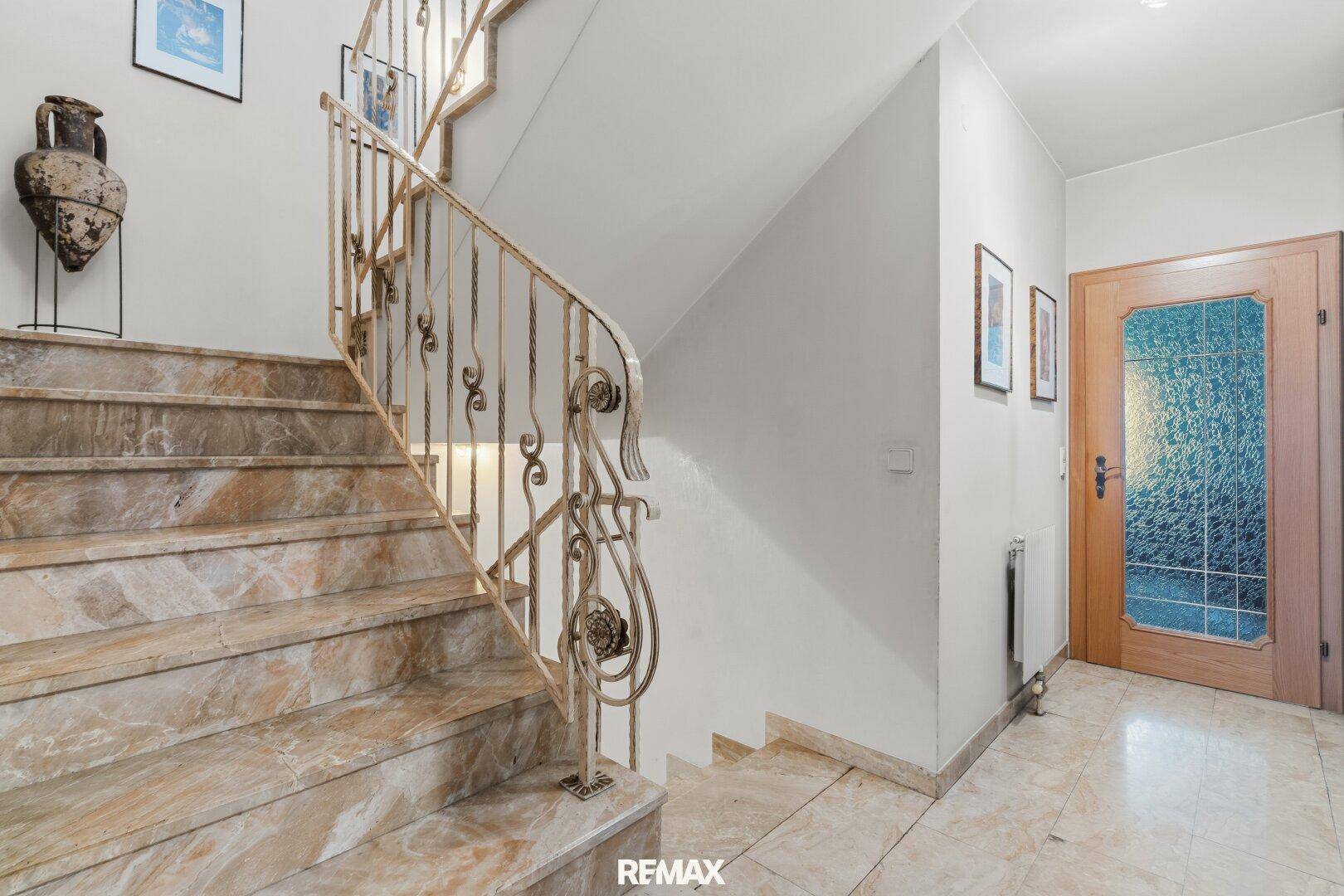 Elegante Marmortreppe mit schmiedeeisernem Geländer und Fliesenboden.