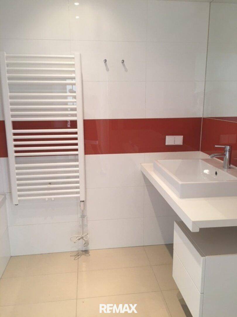 Modernes Badezimmer mit weißen und roten Fliesen, Einzelwaschbecken und Handtuchheizkörper.