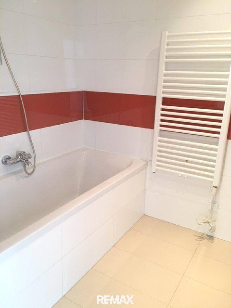 Badezimmer mit Badewanne, Duschvorrichtung, roten Akzentfliesen und Handtuchheizkörper.