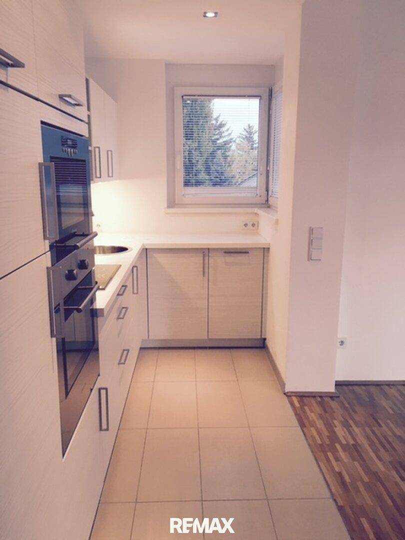 Moderne Küchenzeile mit integrierten Geräten, Fenster und Fliesenboden.