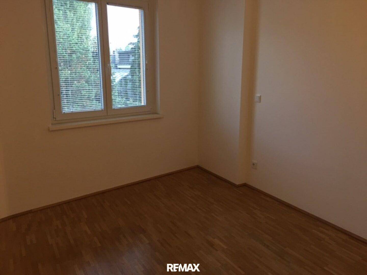 Helles Schlafzimmer mit Parkettboden und Fenster mit Blick ins Grüne.