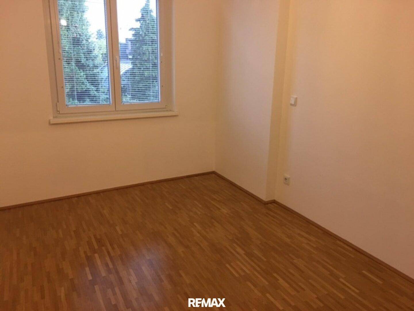 Geräumiges Zimmer mit Holzparkett und großem Fenster für viel Tageslicht.
