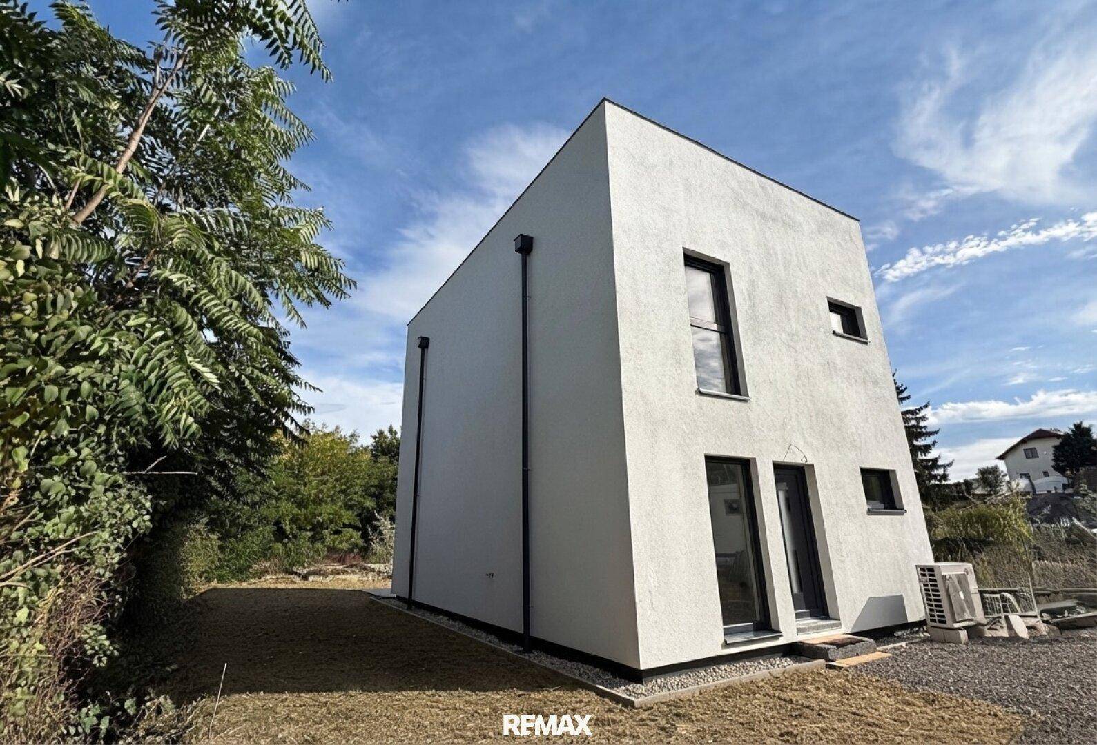 Seitenansicht des modernen Hauses mit weißer Fassade und Klimaanlage im Außenbereich.