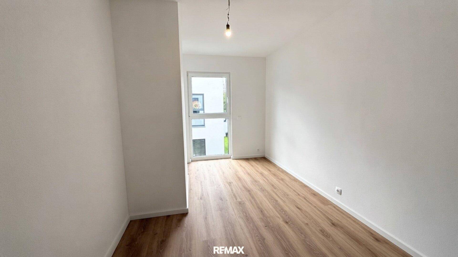 Leeres Zimmer mit Laminatboden und weiß gestrichenen Wänden, mit Zugang nach draußen.