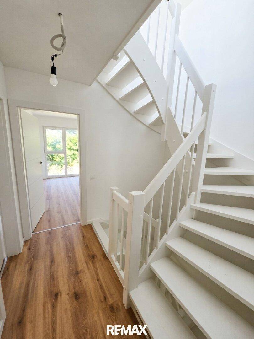 Heller Flur mit Laminatboden und einer modernen weißen Holztreppe, die in die oberen Stockwerke führt.