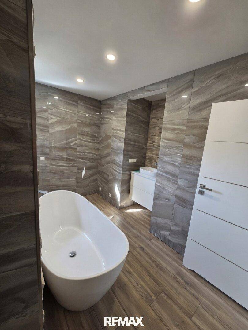 Modernes Badezimmer mit freistehender Badewanne, großformatigen Fliesen und Holzoptik-Boden.