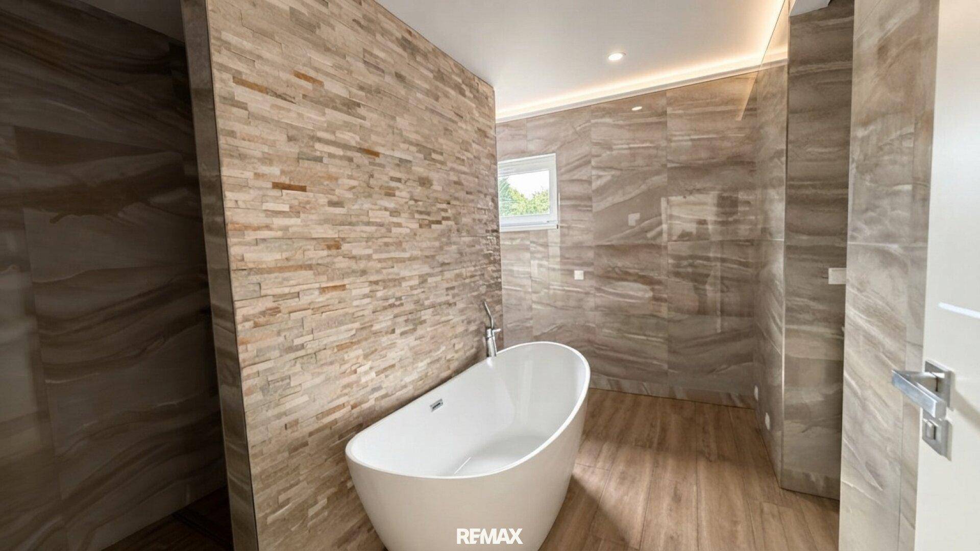 Geräumiges Badezimmer mit freistehender Wanne, Fenster und einer Akzentwand aus Naturstein.