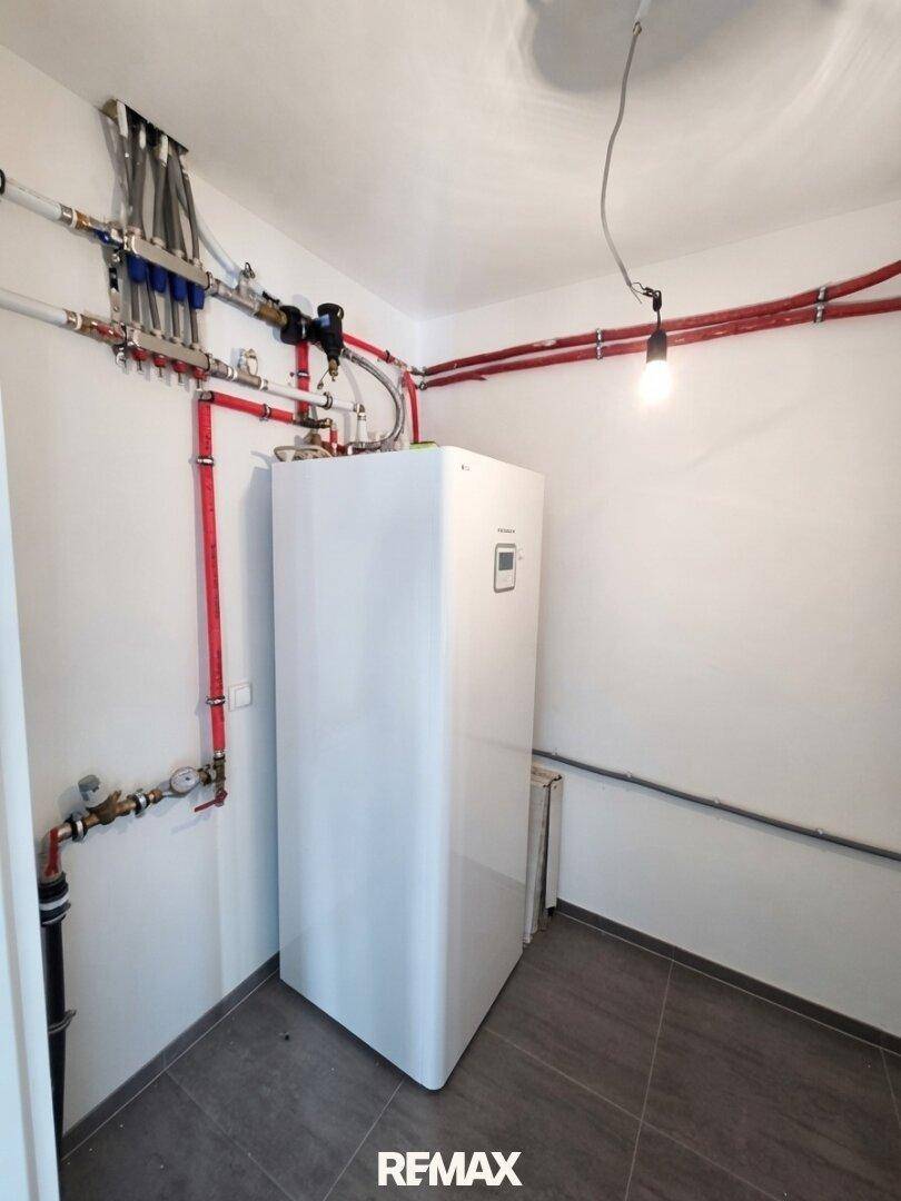 Hauswirtschaftsraum mit Warmwasserspeicher und Heizungsinstallationen auf dunklem Fliesenboden.