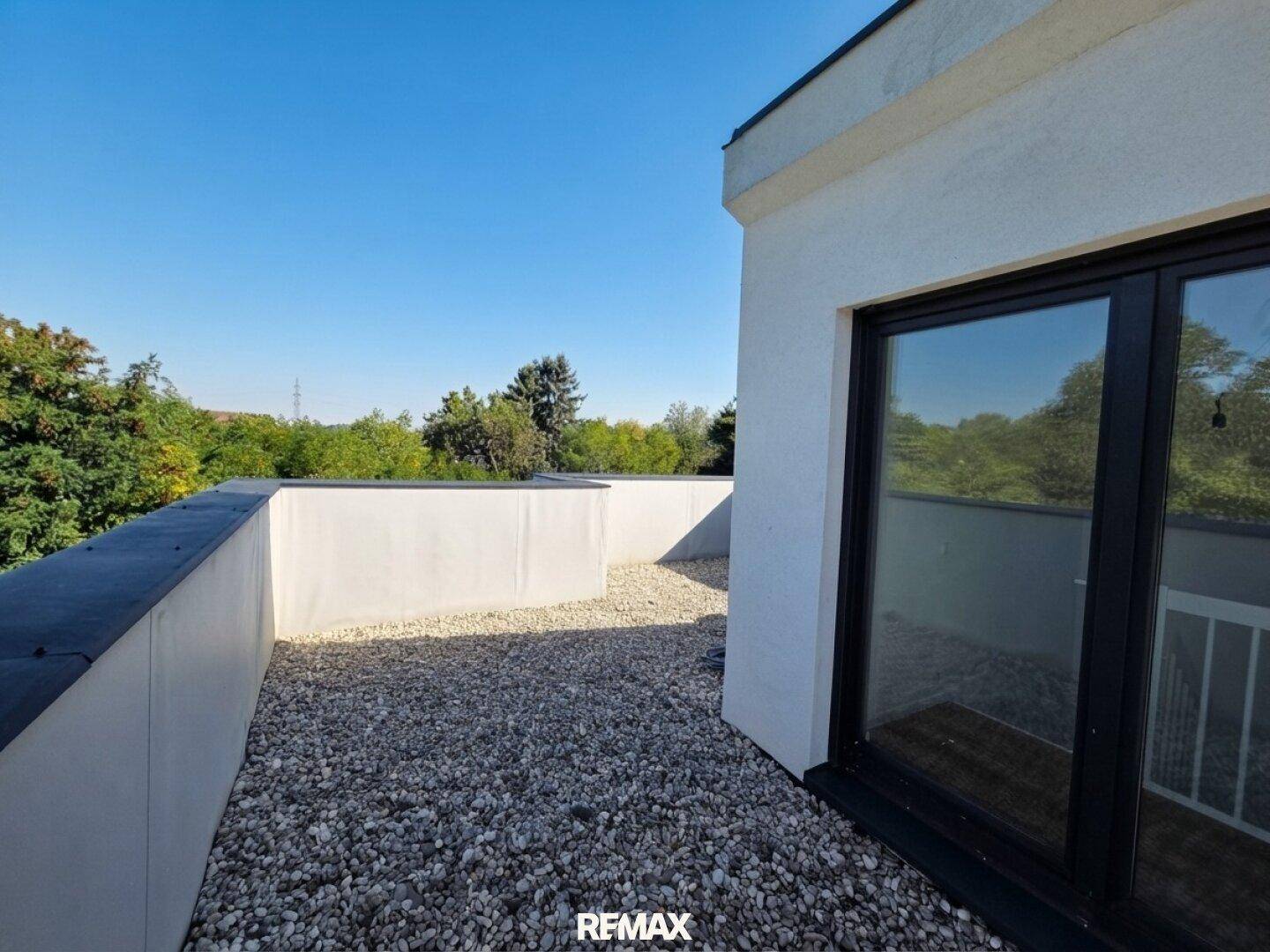 Geräumige Dachterrasse mit Kiesbelag und hohen Brüstungsmauern, ideal zum Entspannen.