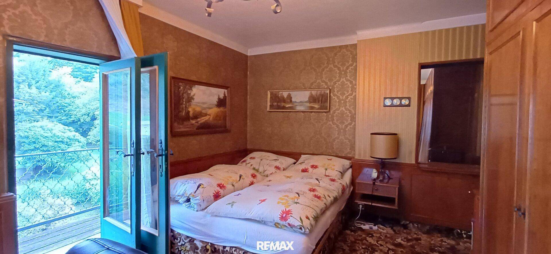Gemütliches Schlafzimmer mit traditioneller Tapete, Holzmöbeln und direktem Zugang zum Balkon.