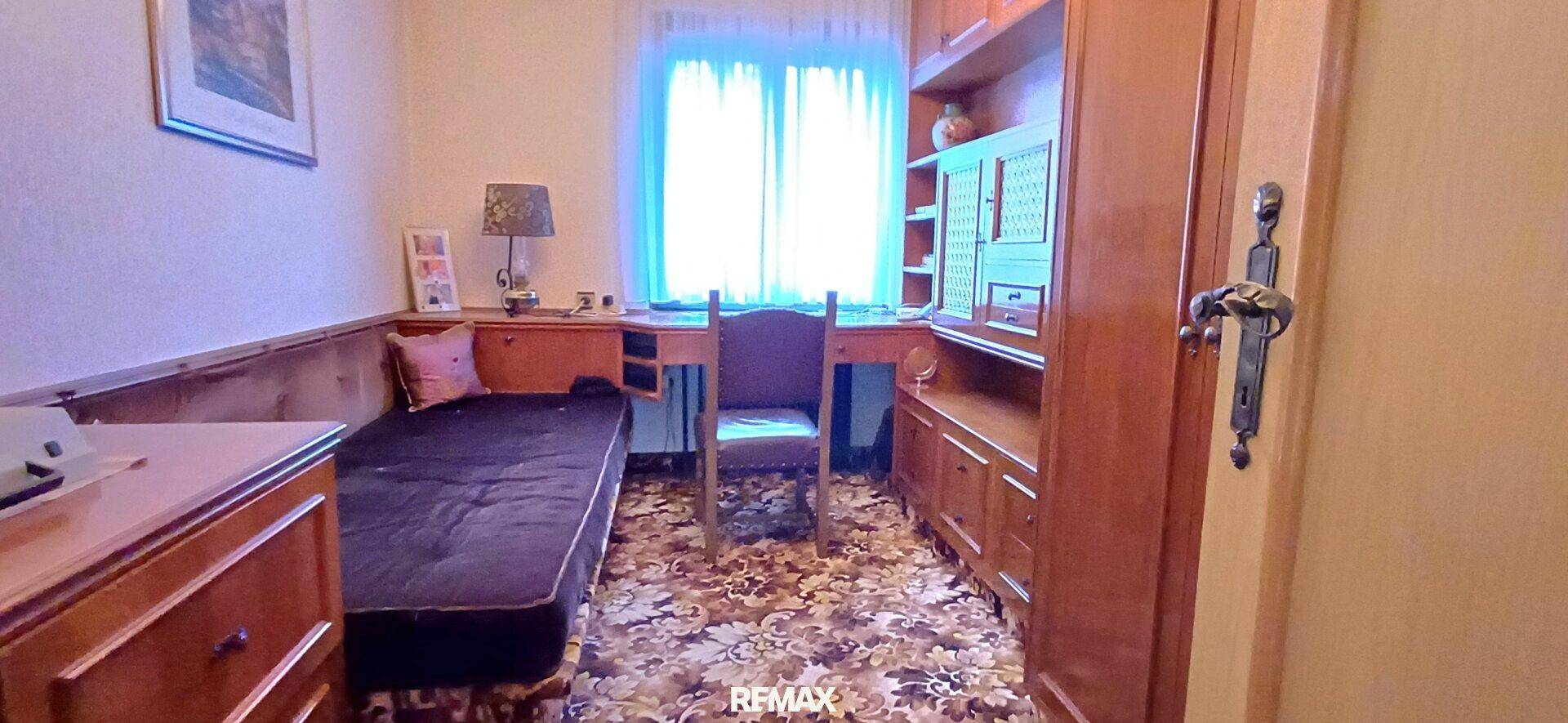 Kleines Schlafzimmer oder Arbeitszimmer mit Einzelbett, Holzregalen und gemustertem Teppichboden.