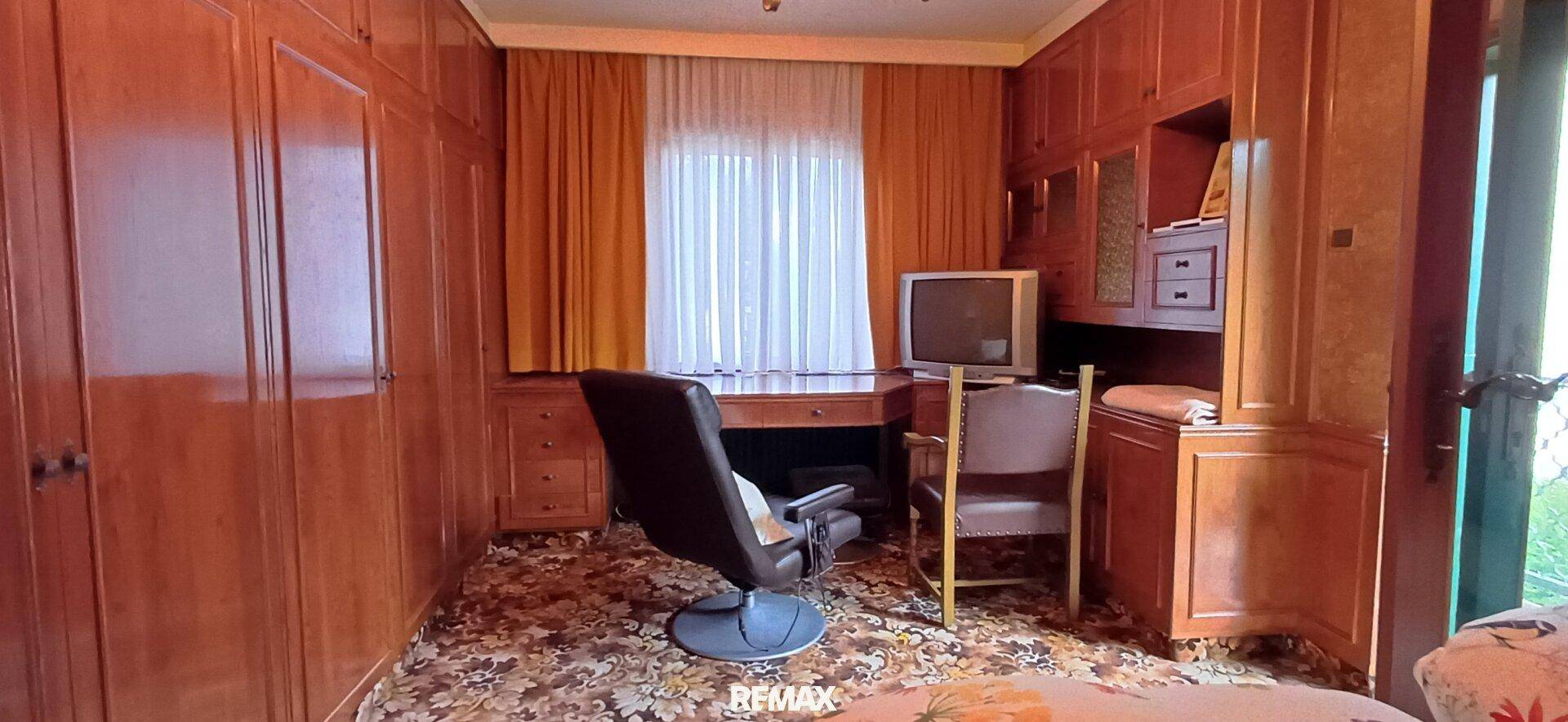 Arbeitszimmer mit umfassenden Holz-Einbaumöbeln, Schreibtisch und einem Fernseher, ideal für Home-Office.