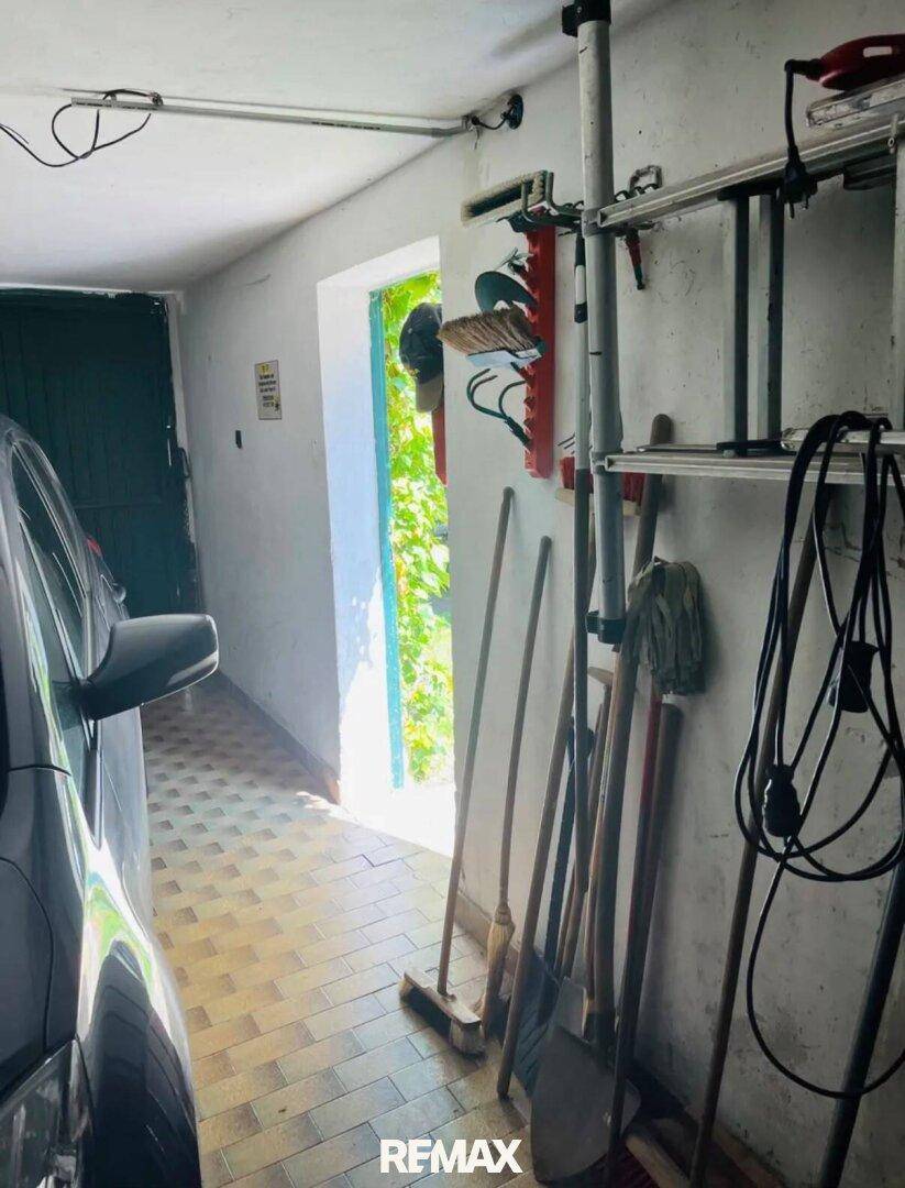 Geräumige Garage mit einem Auto, Werkzeugen und einem offenen Tor, das ins Freie führt.