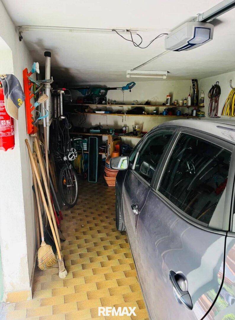 Garage mit einem geparkten Auto, Regalen voller Werkzeuge und einem Fahrrad, bietet viel Stauraum.