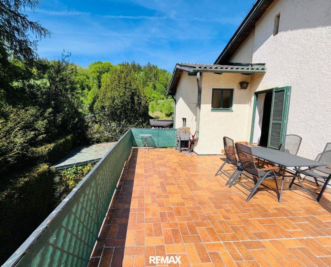 Großzügige Terrasse mit Terrakotta-Fliesen, Gartenmöbeln und Blick auf die umliegende Natur.