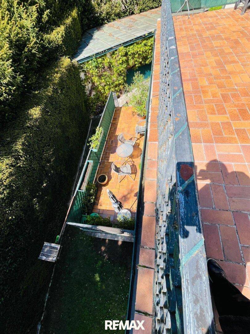 Blick von oben auf eine untere Terrasse mit Gartenmöbeln und umgeben von grünen Hecken.