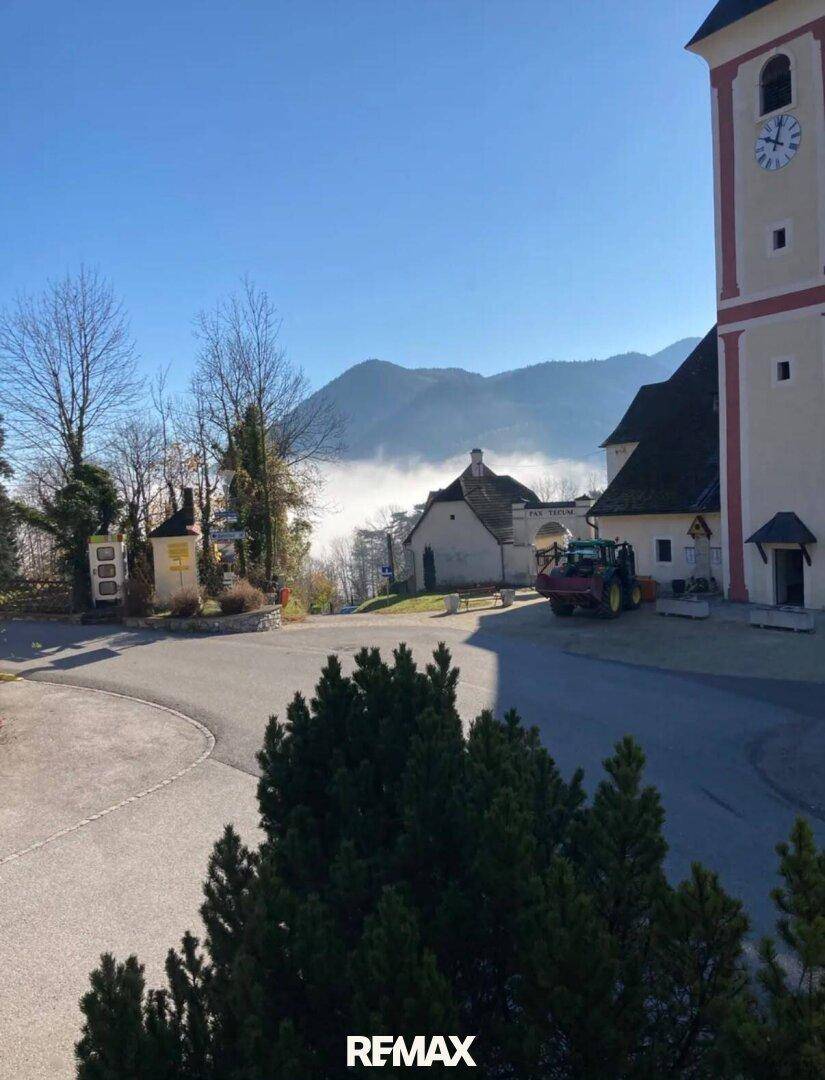 Dorfansicht mit Kirchturm, Bergen und Nebel im Tal an einem sonnigen Wintertag.