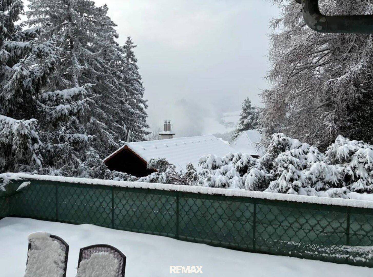 Schneebedeckte Terrasse mit Gartenstühlen und weitem Blick über winterliche Bäume und die Landschaft.