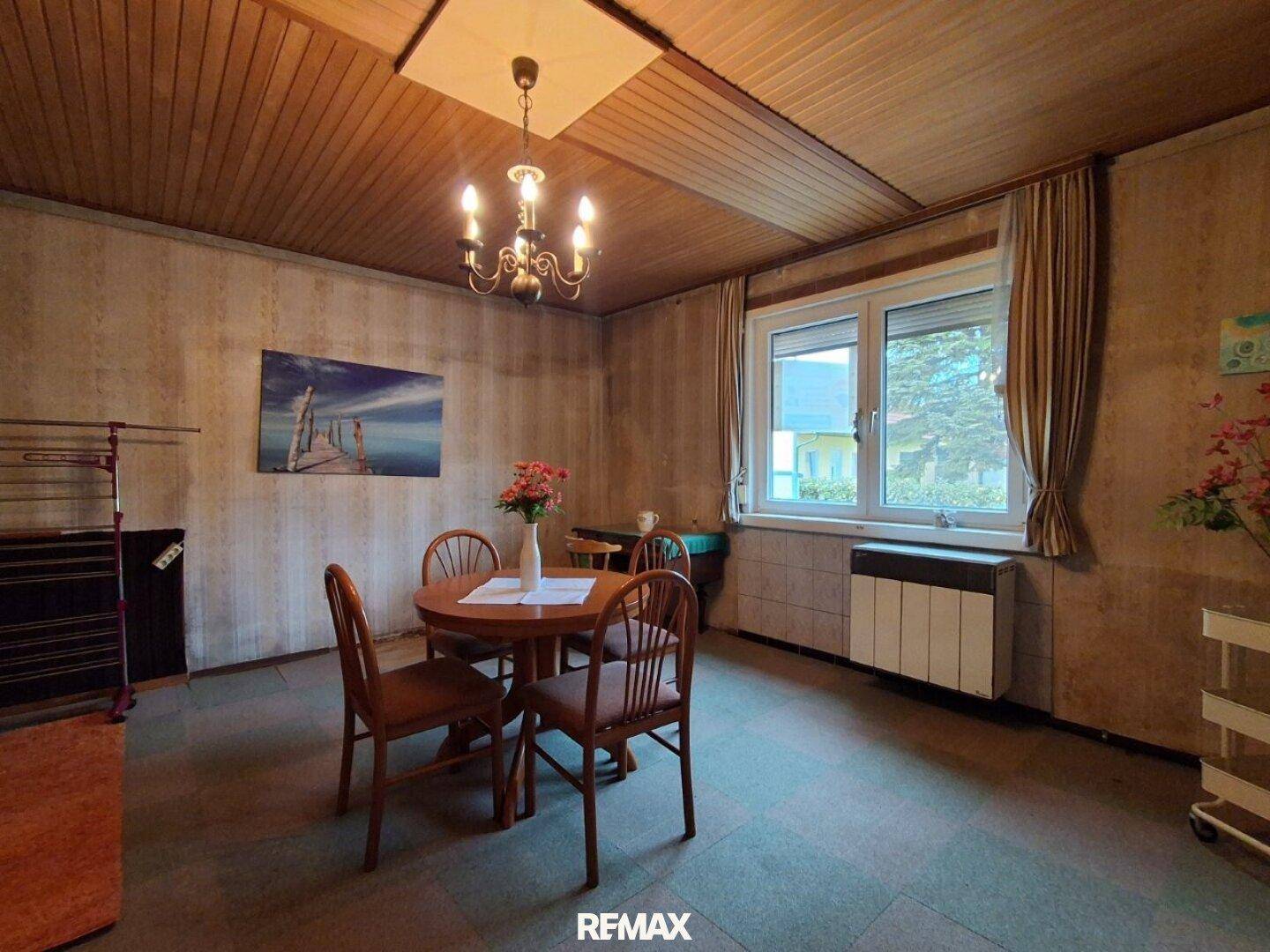 Wohnraum mit Holztisch, Stühlen, Fenster und rustikaler Holzdeckenverkleidung.