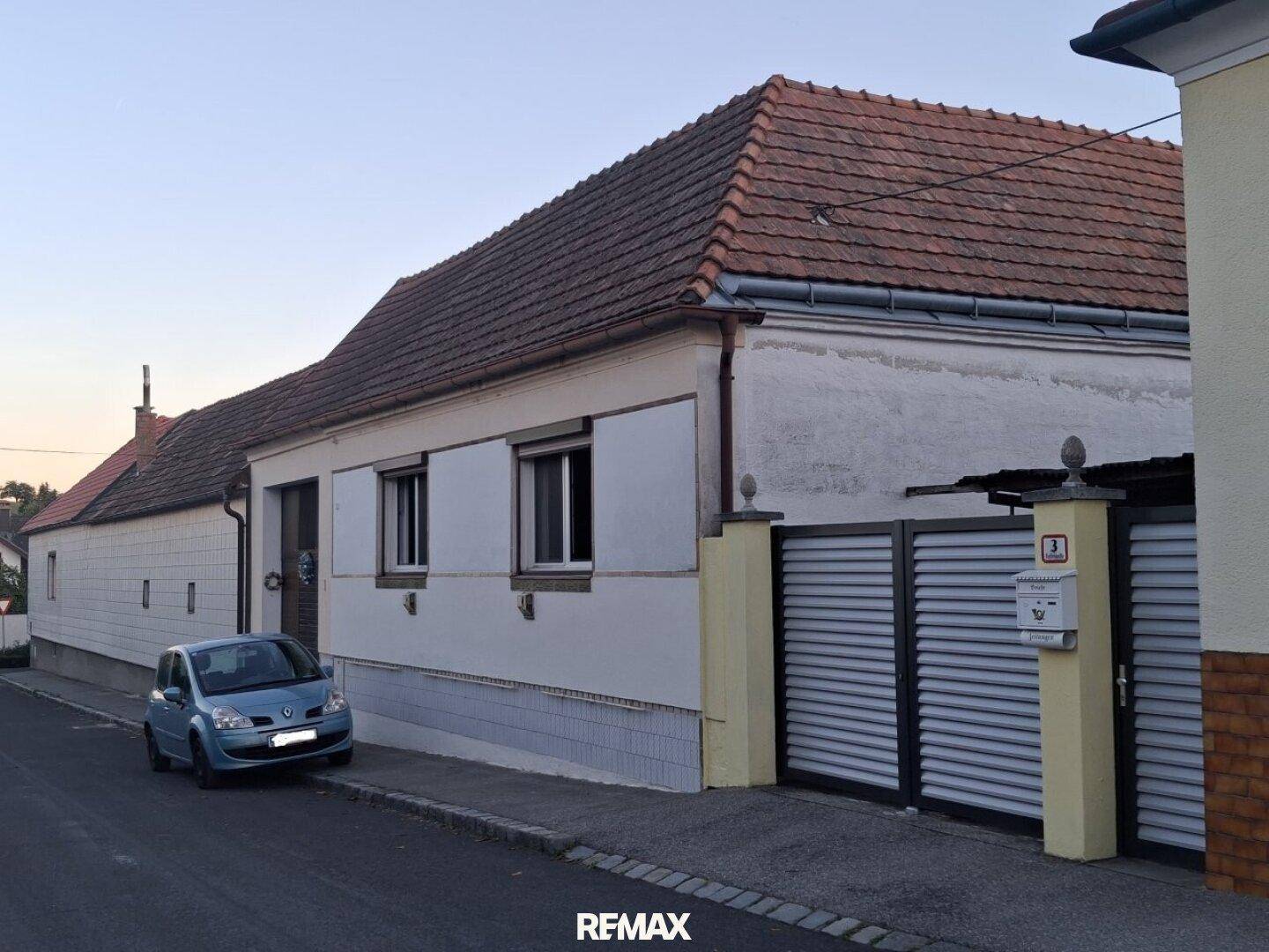 Fassade eines traditionellen Hauses an der Straße mit Einfahrtstor und geparktem Auto.