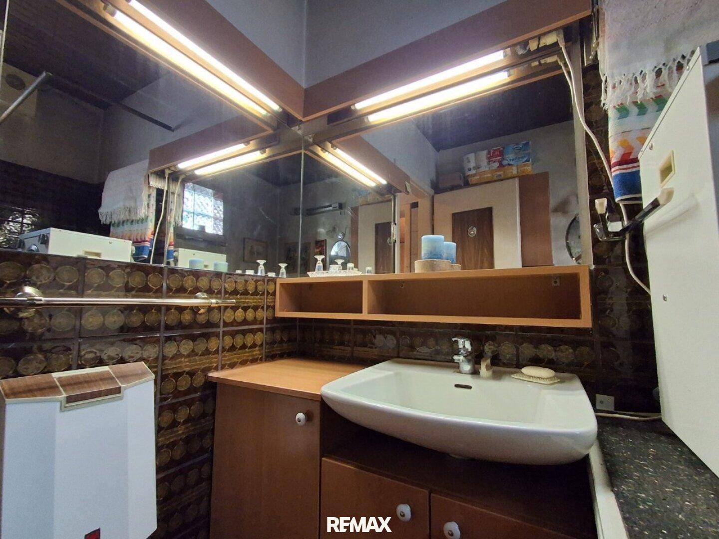 Badezimmer mit Waschbecken, großem Spiegelschrank und braunen Fliesen an den Wänden.