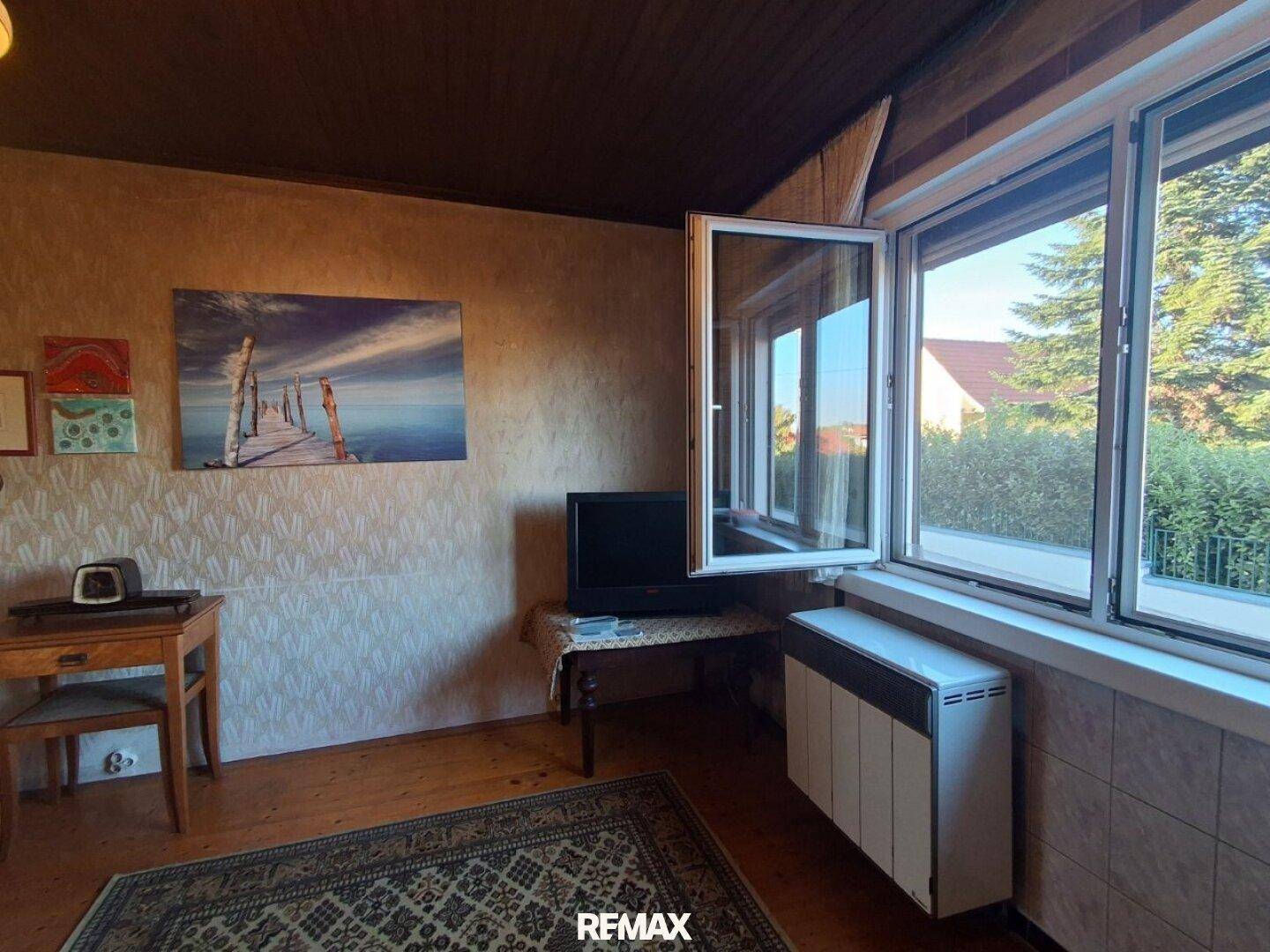 Heller Wohnraum mit geöffnetem Fenster, Fernseher und Holzboden, der viel Tageslicht hereinlässt.
