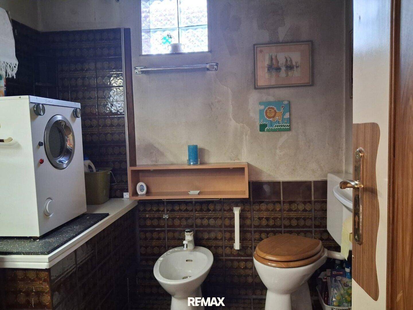 Badezimmer mit Toilette, Bidet und Waschmaschine, ausgestattet mit braunen Wandfliesen.