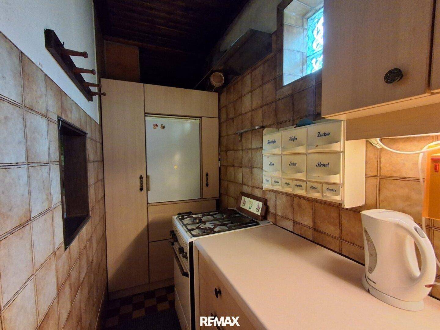 Küche mit Gasherd, Kühlschrank und braunen Wandfliesen, funktional eingerichtet.