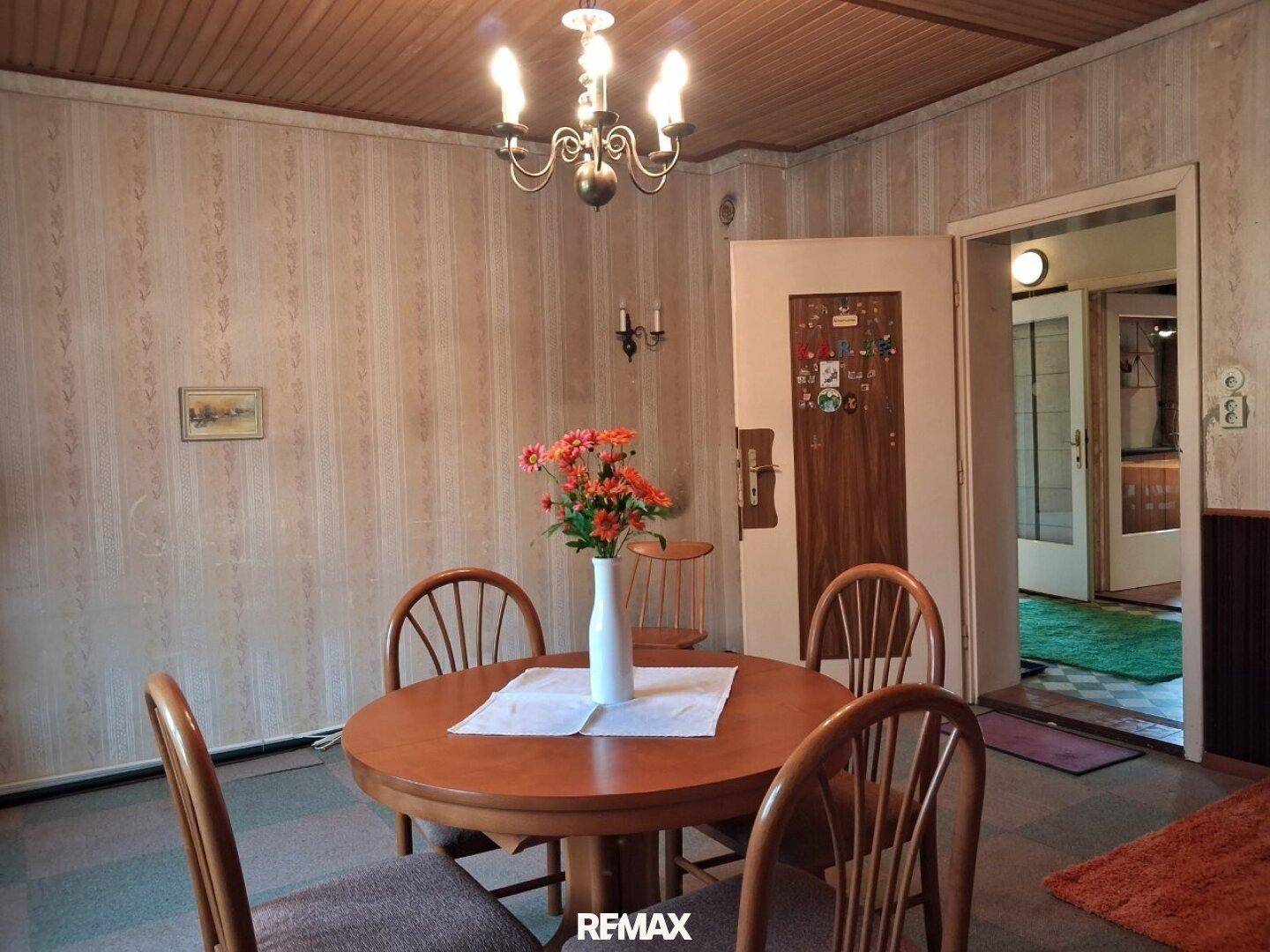 Esszimmer mit rundem Holztisch, Stühlen und gemusterter Tapete, mit Zugang zum Flur.