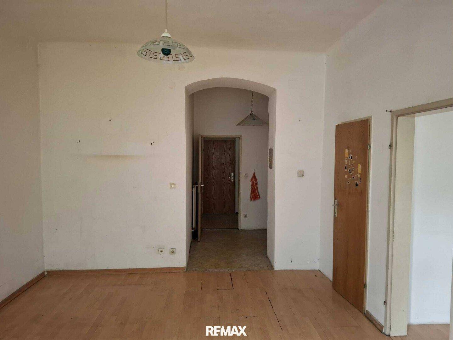 Leeres Wohnzimmer mit Holzboden und einem Rundbogen, der zu einem weiteren Raum führt.