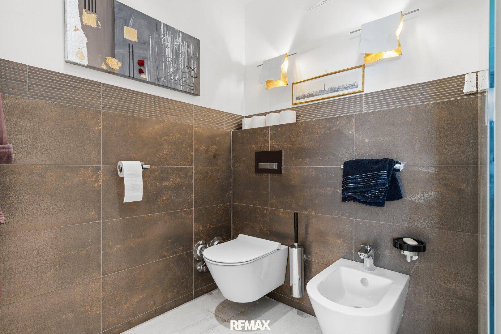 Separates WC mit Wand-WC, Bidet und modernen braunen Wandfliesen.