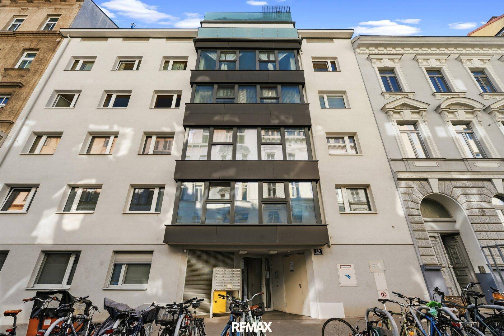 Vorderansicht eines Wohnhauses mit mehreren Etagen und Fahrradstellplätzen.