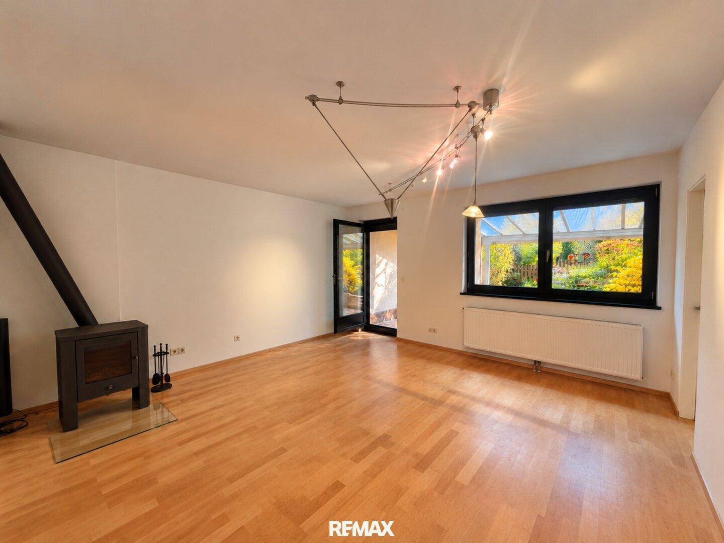 Helles Wohnzimmer mit Holzofen, Parkettboden und Zugang zu einem Außenbereich.
