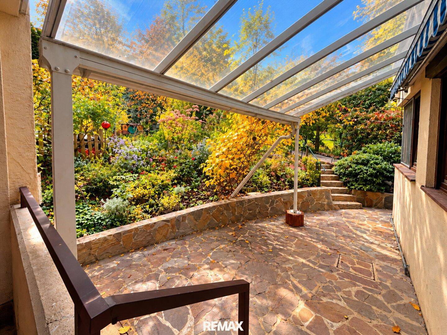 Überdachte Terrasse mit Steinboden und Blick auf den herbstlichen Garten.