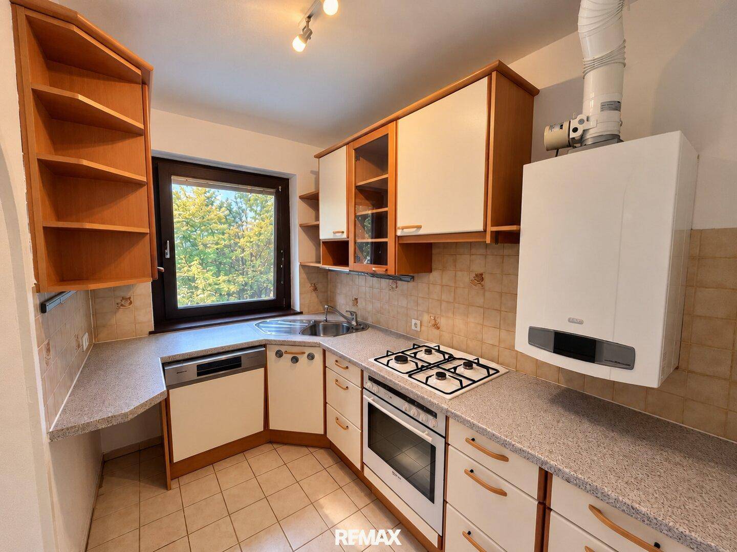 Funktionale Küche mit Gasherd, Einbauschränken und Fenster mit Blick ins Grüne.