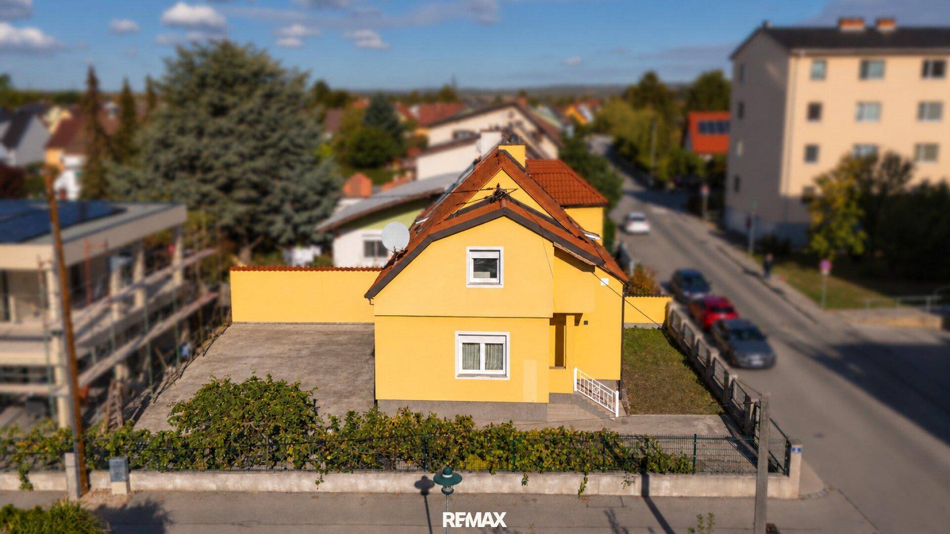 Rückansicht des gelben Hauses mit gepflastertem Hofbereich und angrenzender Wohnbebauung.