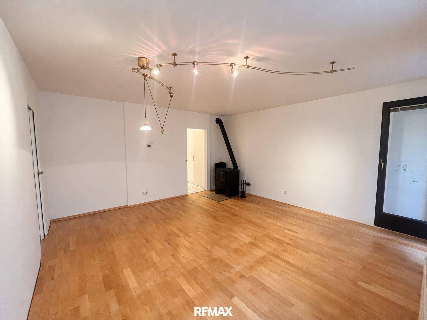 Wohnzimmer mit Holzofen und Parkettboden, bietet direkten Zugang zum Außenbereich.