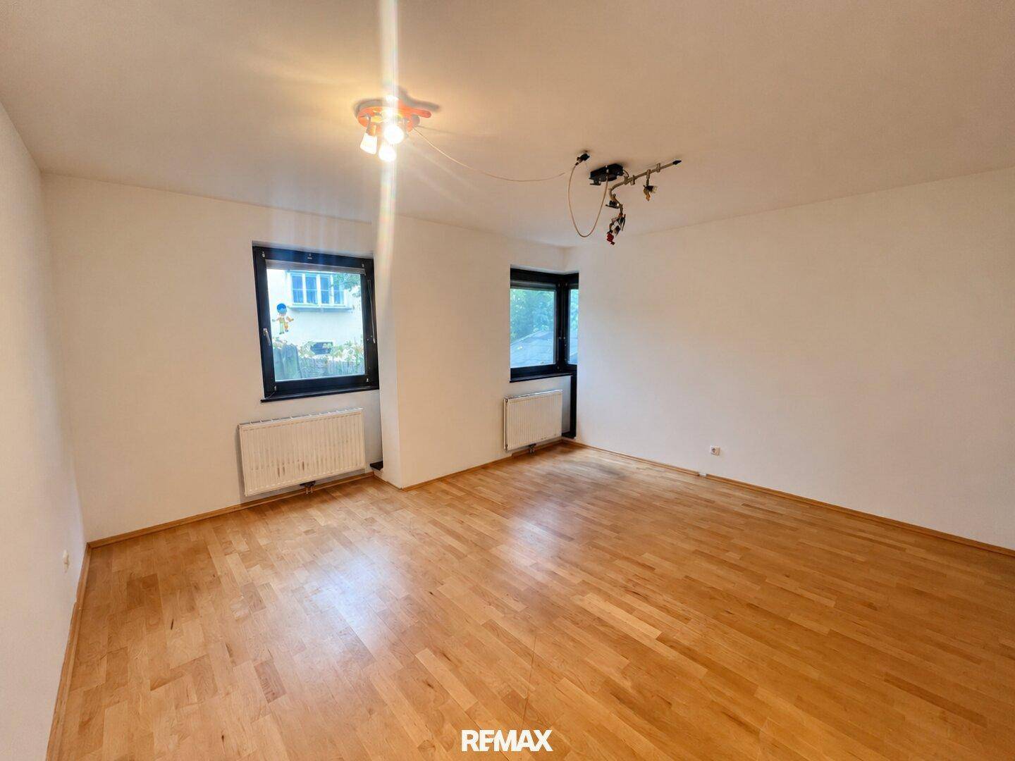 Helles Zimmer mit Parkettboden und zwei Fenstern, die eine angenehme Atmosphäre schaffen.