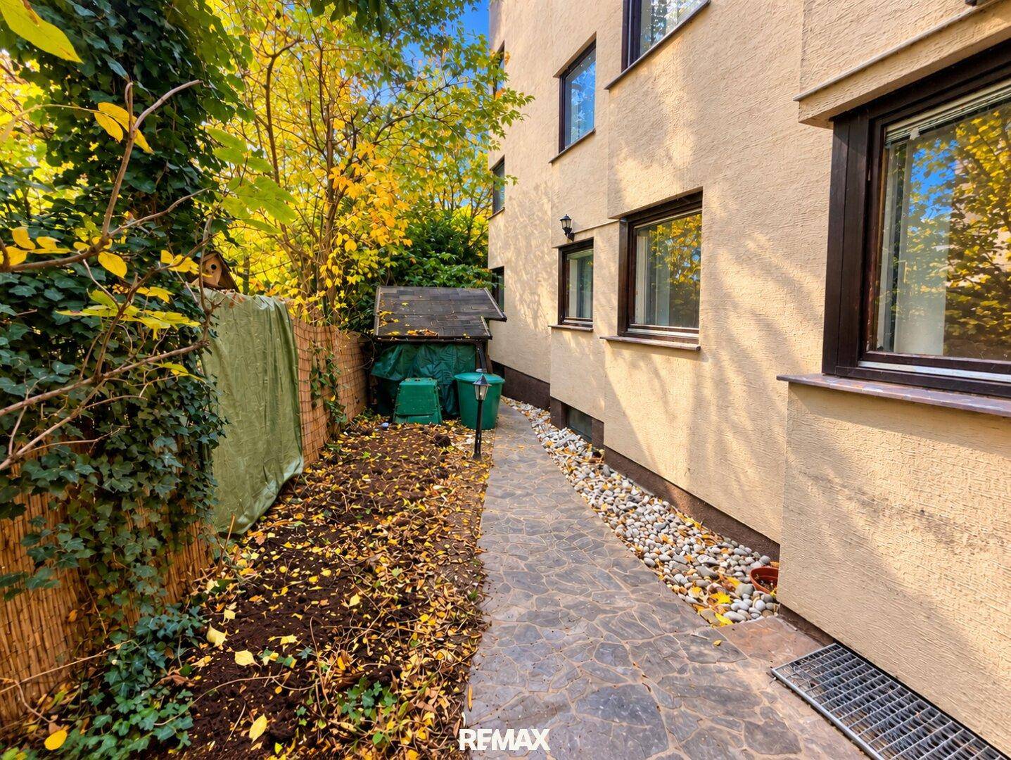 Seitenansicht des Gebäudes mit einem schmalen Weg und herbstlichem Laub.