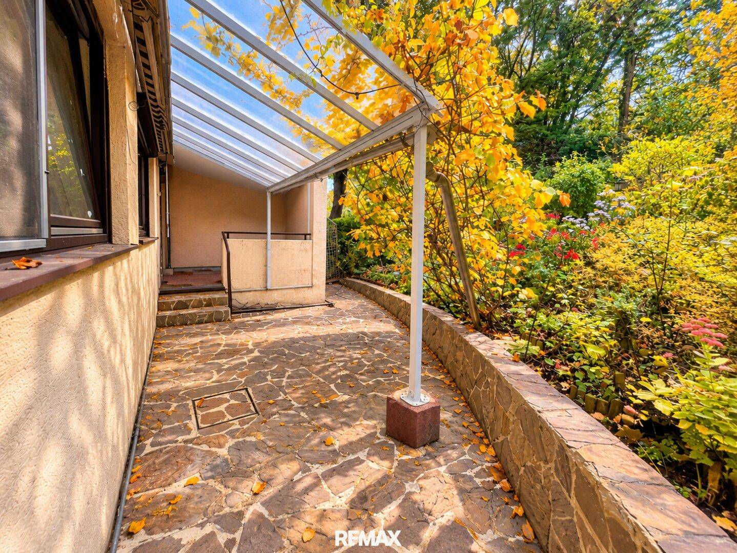 Überdachte Terrasse mit Steinboden und direktem Zugang zum Gartenbereich.