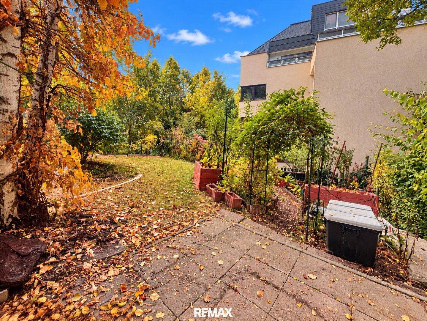 Gartenbereich mit Rasenfläche, herbstlichem Laub und Blick auf das Gebäude.
