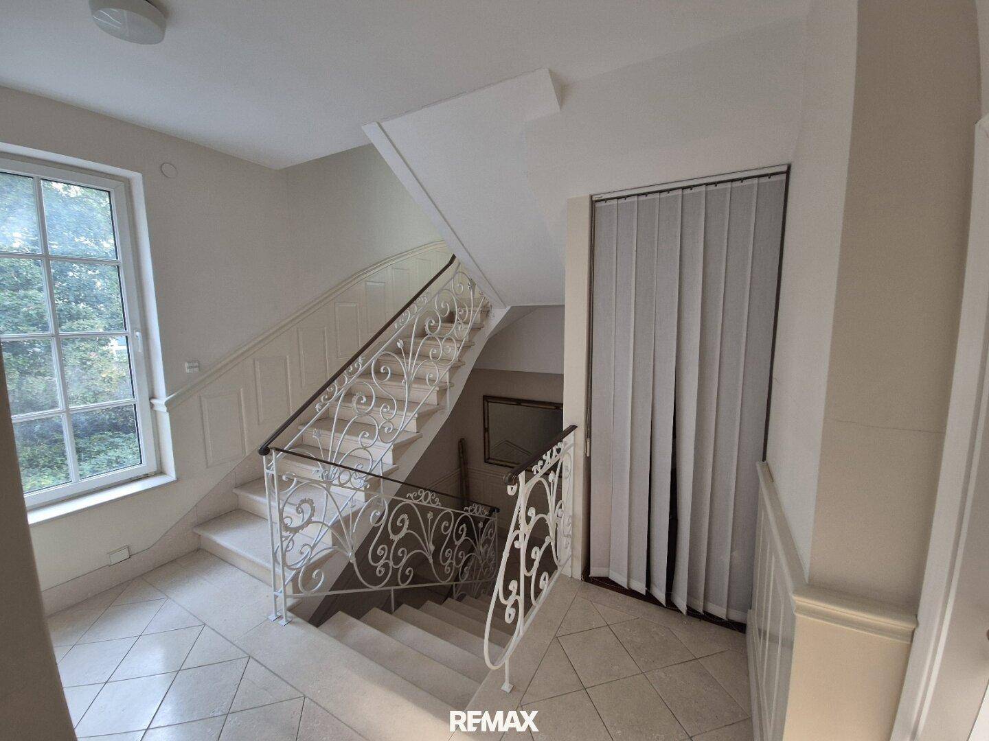 Geräumiger Flur mit eleganter Treppe, schmiedeeisernem Geländer und großem Fenster.