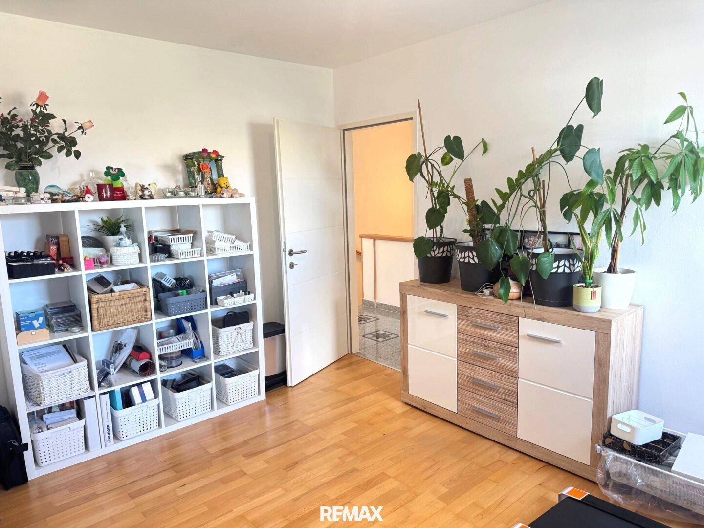 Helles Zimmer mit Holzboden, Bücherregal und vielen Pflanzen, ideal als Schlaf- oder Arbeitszimmer.
