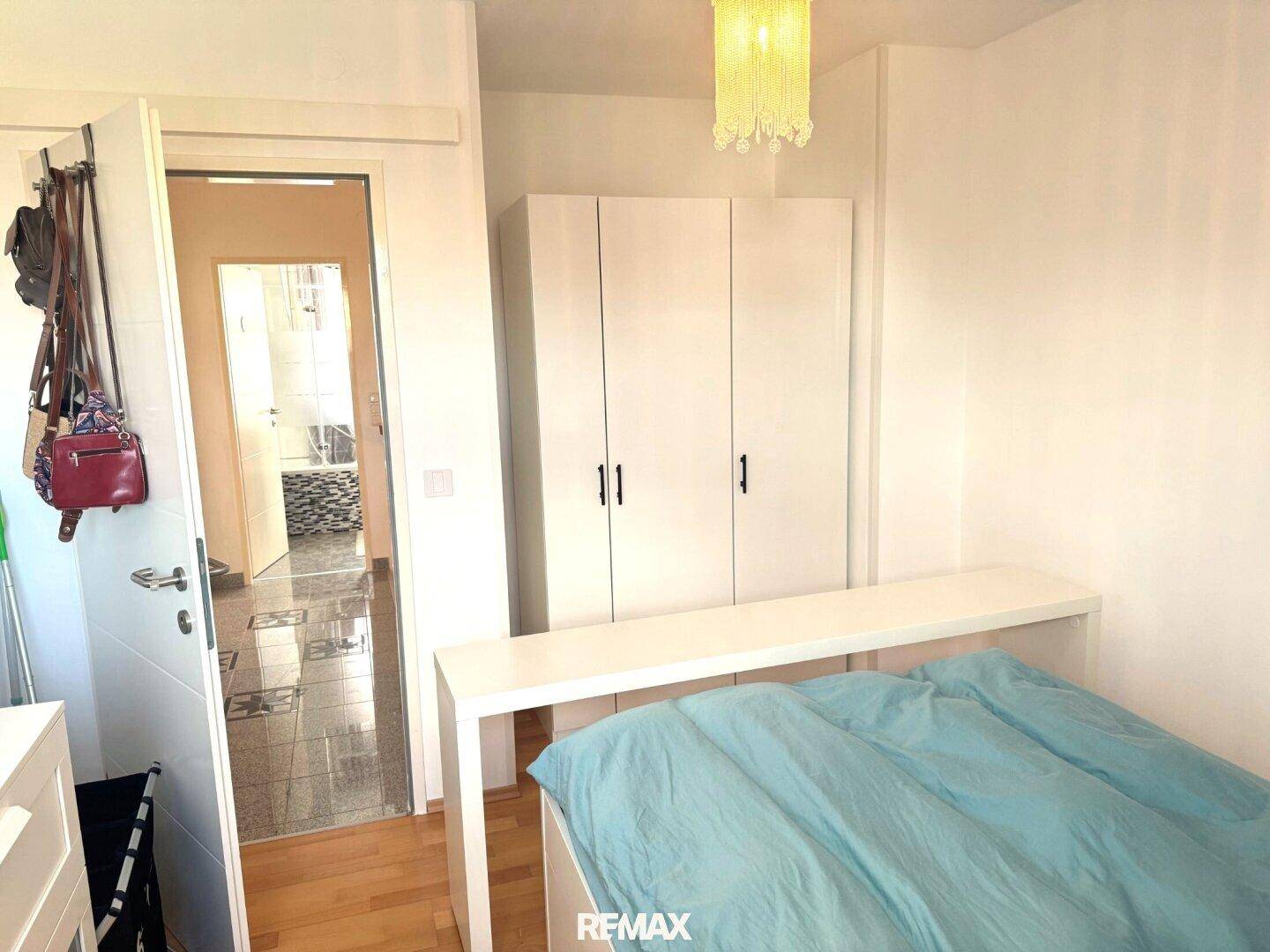 Helles Schlafzimmer mit Einzelbett und weißem Kleiderschrank, mit Blick auf den Flur.