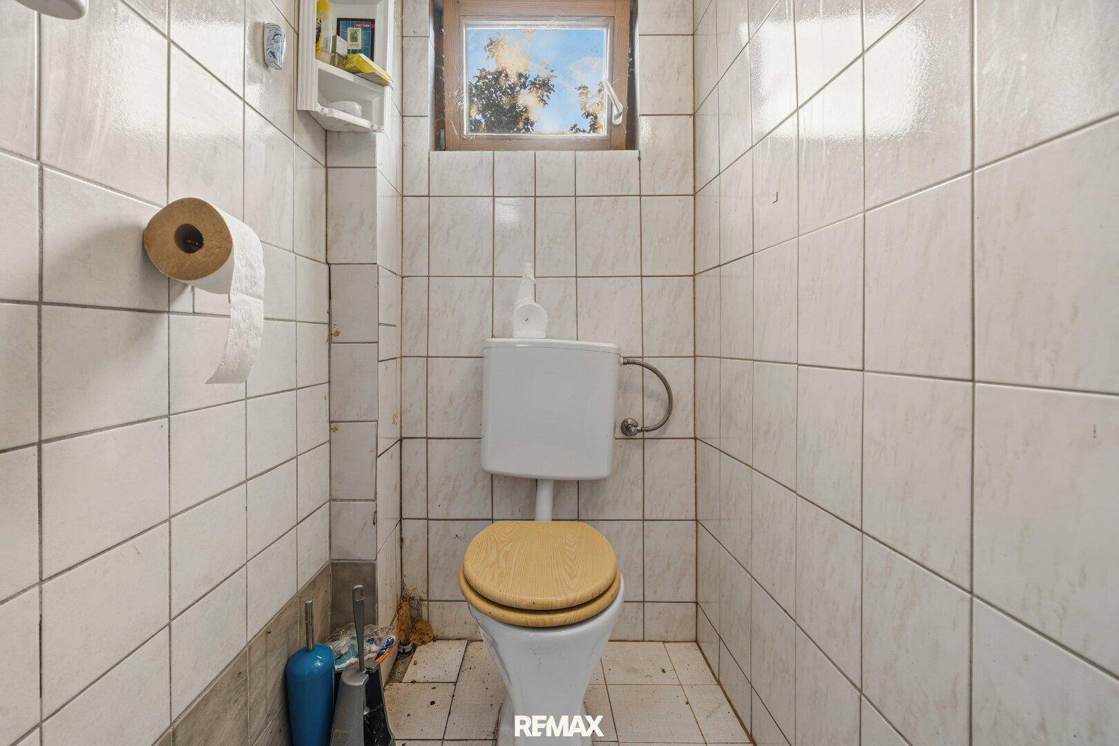 Kleines WC mit weißen Fliesen, Toilette und einem Fenster für natürliche Belüftung.