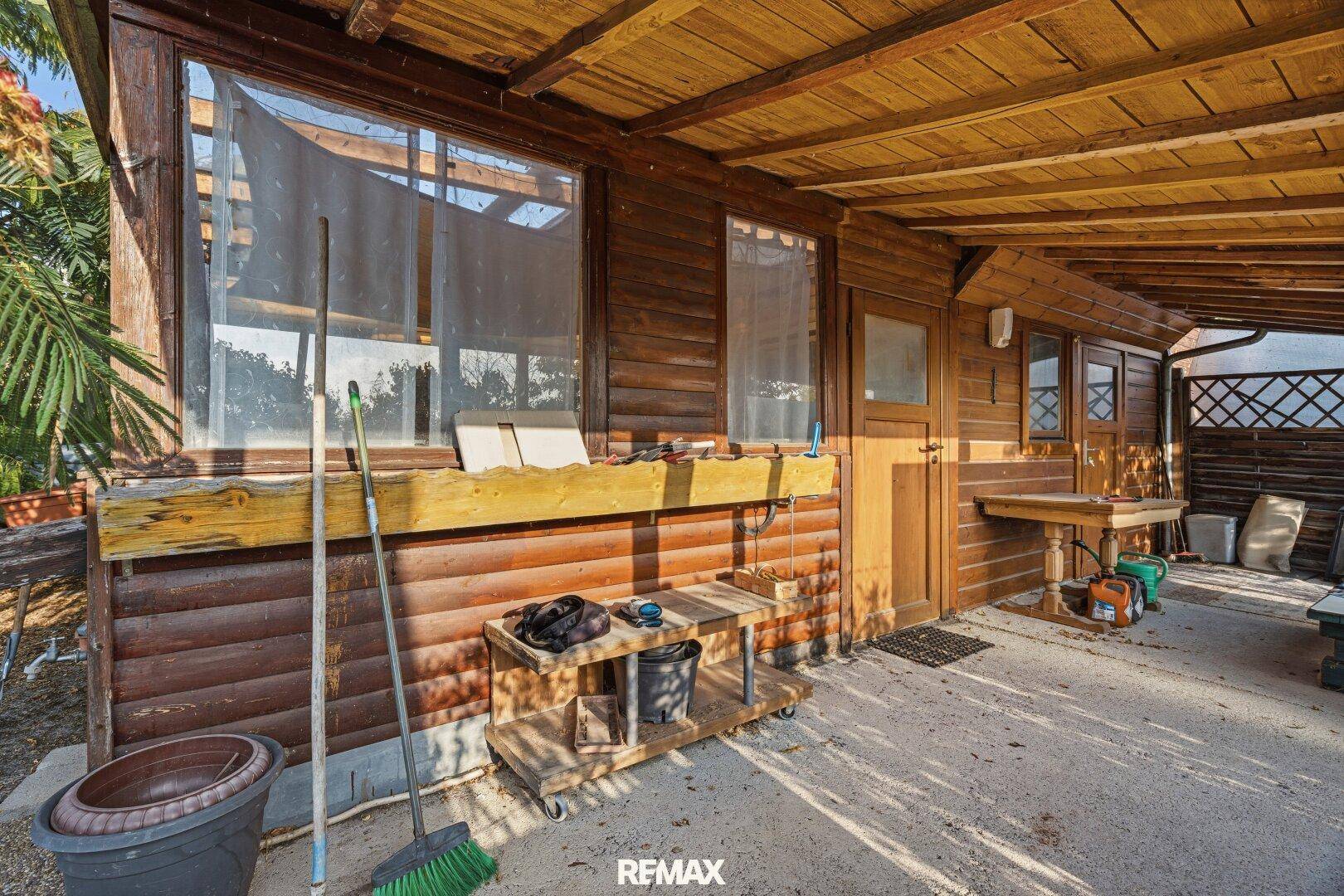 Überdachte Terrasse am Holzhaus mit Blick auf den Garten und einfachem Mobiliar.