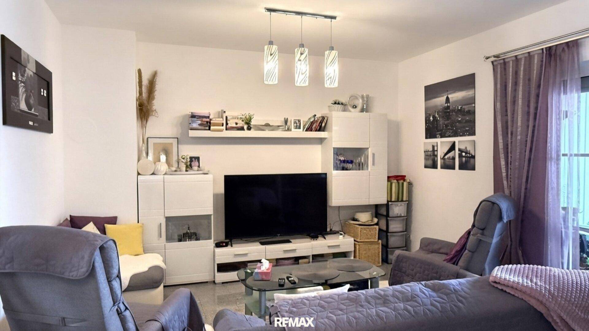 Gemütliches Wohnzimmer mit Sofa, Fernseher und modernen Hängelampen, ideal zum Entspannen.