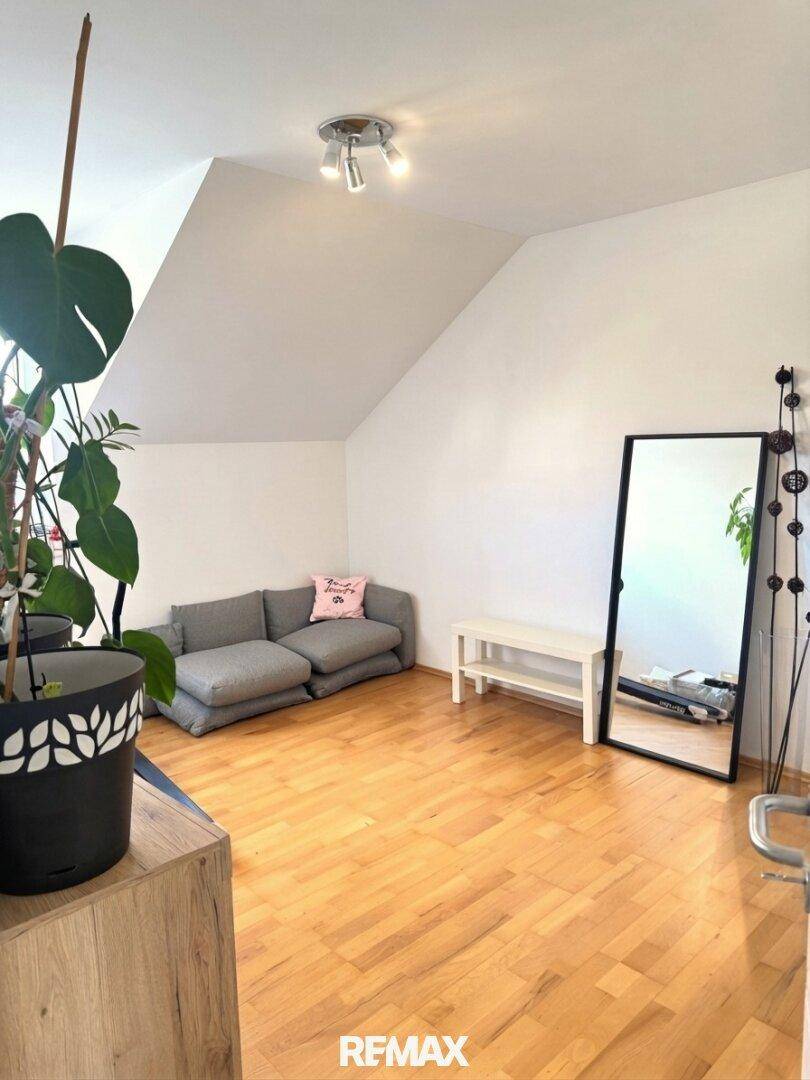 Helles Zimmer im Dachgeschoss mit Holzboden, kleiner Couch und großem Spiegel.