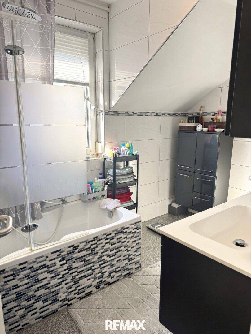 Badezimmer im Dachgeschoss mit Badewanne, Duschvorhang und Einzelwaschbecken.